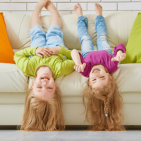 Two little girls hanging off the couch upside down