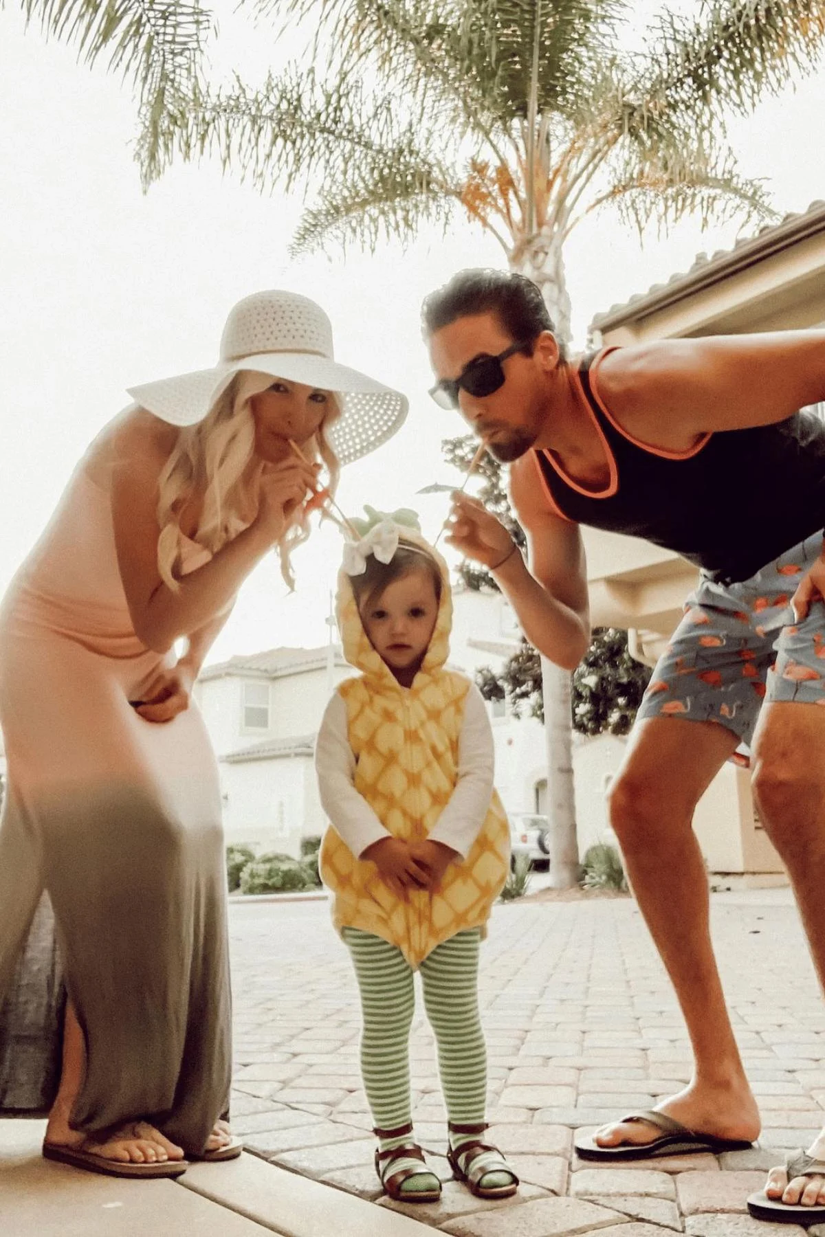 Mom and dad dressed like tourists sipping from a tropical drink (their daughter, a pineapple)