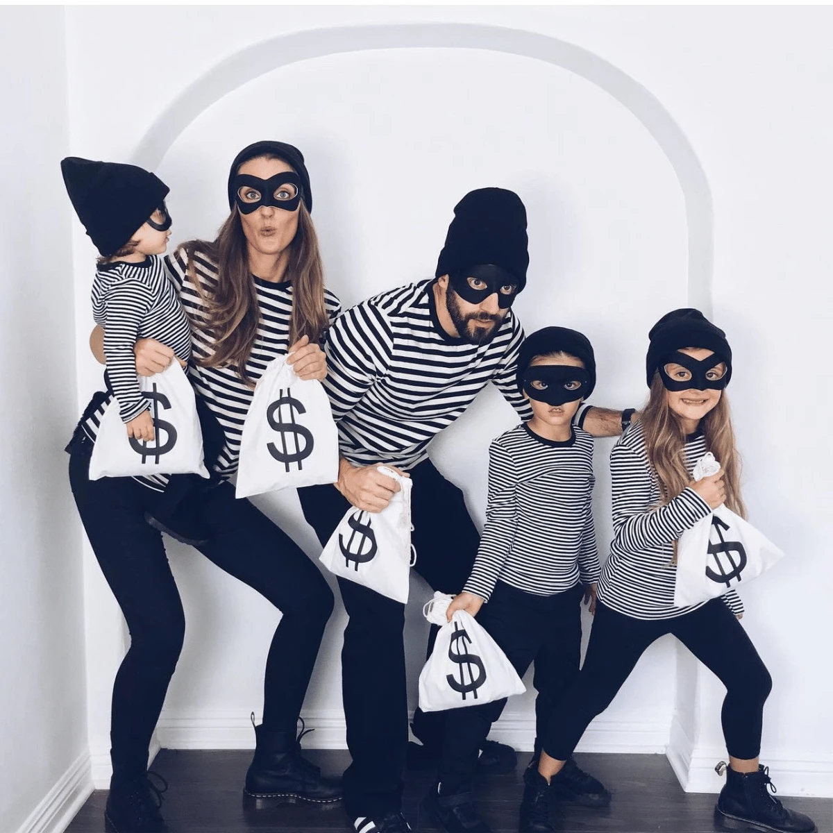 Family of 5 holding bags of money, and wearing face masks, black hats and black and white striped shirts